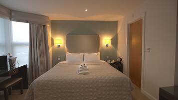 A hotel room with a large bed, two bedside lamps, a desk with a computer, and a window with curtains.