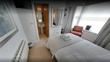 A hotel room with a bed, a window with curtains, a bathroom with a sink and mirror, and a radiator.
