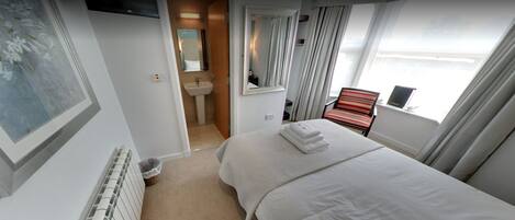 A hotel room with a bed, a window with curtains, a bathroom with a sink and mirror, and a radiator.