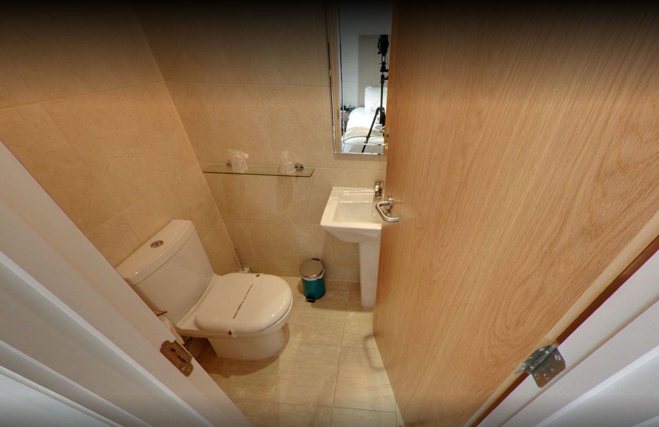 A small, narrow bathroom with a toilet, sink, and mirror.