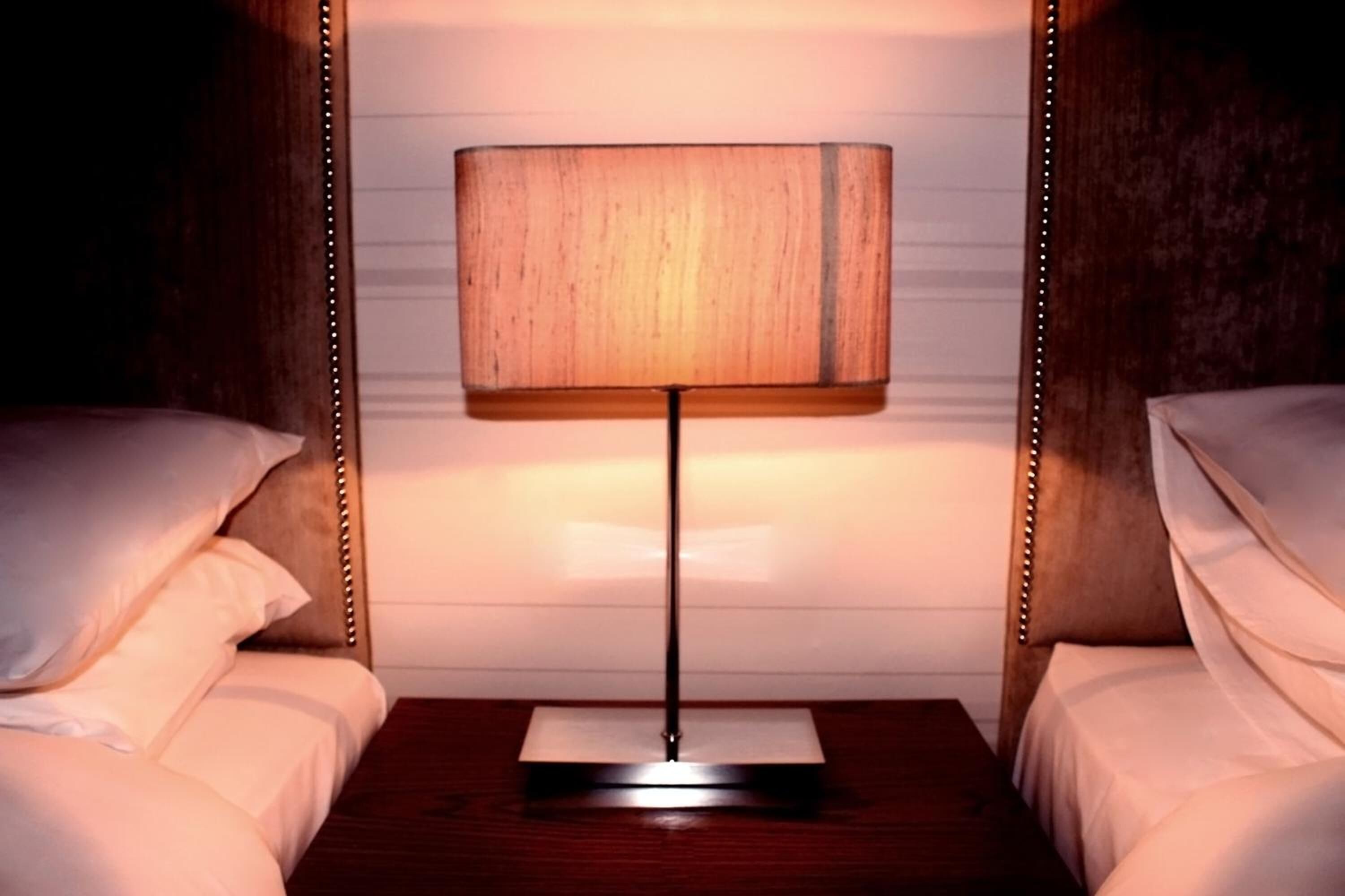 Ein Hotelzimmer mit zwei Betten, einem Nachttisch aus Holz mit einer Lampe und einer weißen Wand.