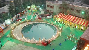 A circular pool with a green carpeted area, surrounded by a decorative railing and string lights. - Hotel Jaipur Ashok (Jaipur)