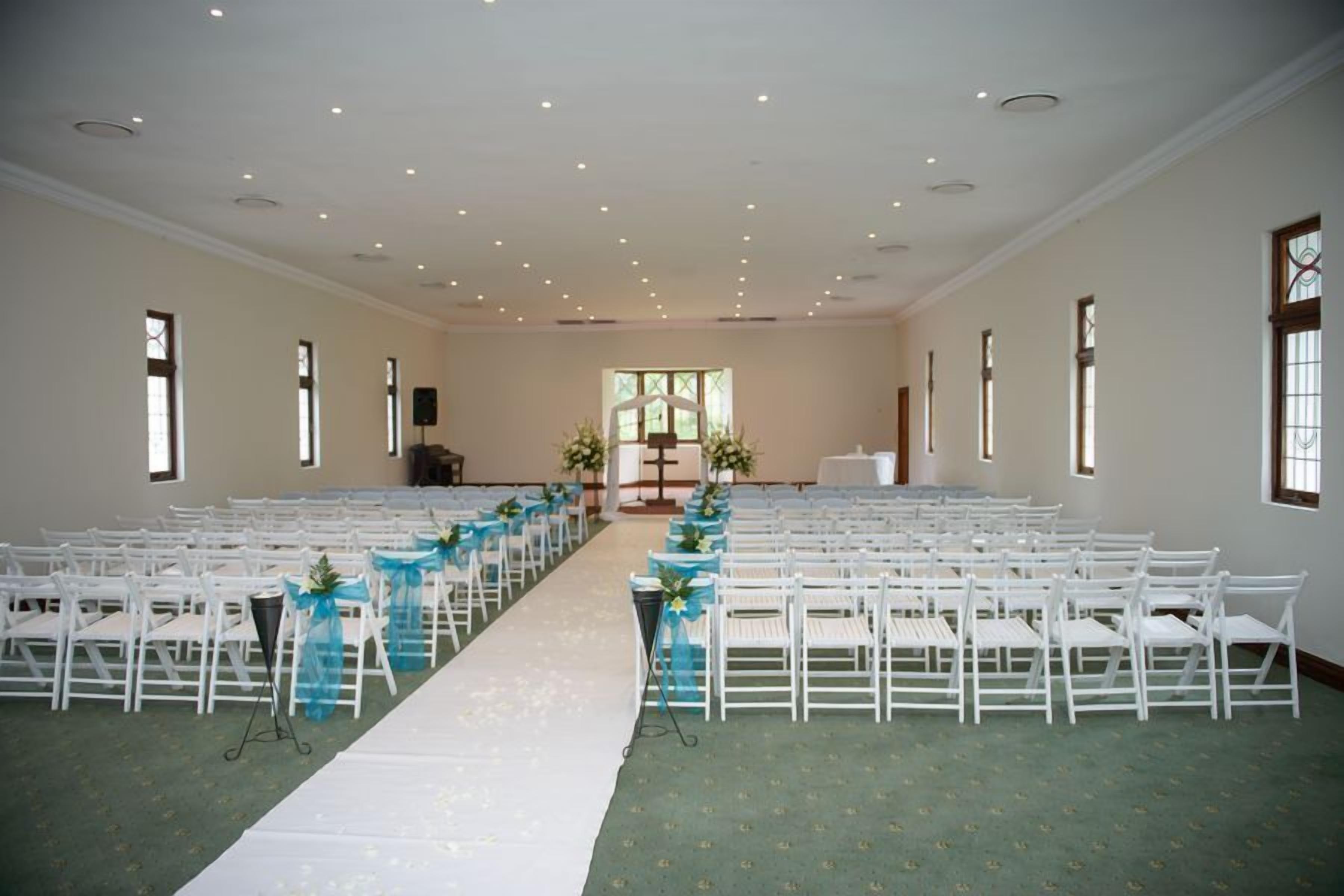 Interior de iglesia con bancas dispuestas en filas, un pasillo blanco y una alfombra verde.
