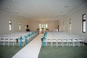 Interior de iglesia con bancas dispuestas en filas, un pasillo blanco y una alfombra verde.
