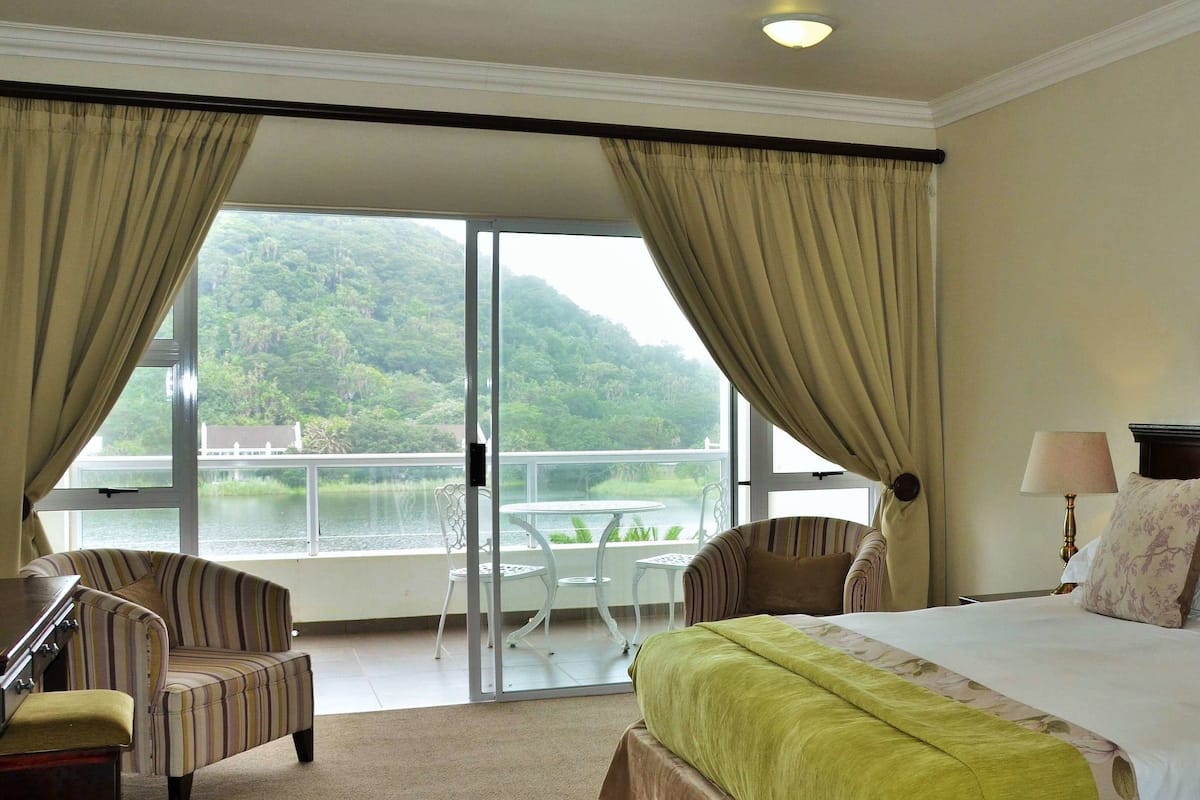 Ein Hotelzimmer mit Bett, zwei Stühlen, einem Tisch und Blick auf See und Wald.