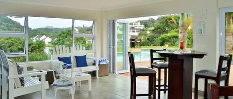 A spacious room with large windows, a pool view, and a bar area.