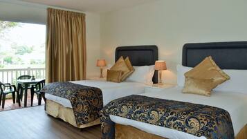A hotel room with two beds, a small table, chairs, and a view of the outdoors.