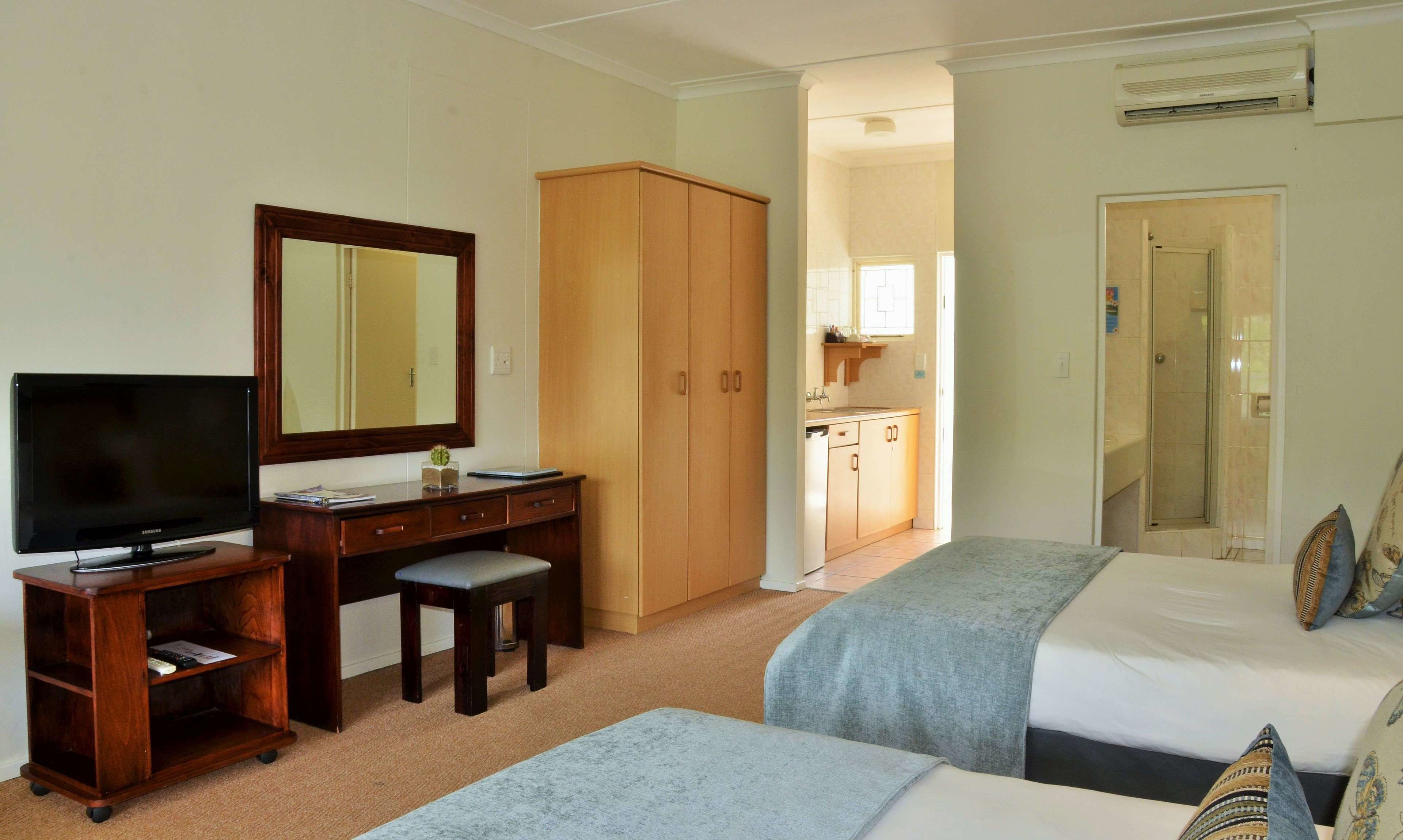A hotel room with a TV, desk, two beds, a wardrobe, and a bathroom visible through an open door.