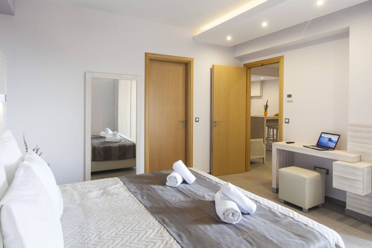 A modern hotel room with a bed, a desk, a chair, and a bathroom visible through an open door.