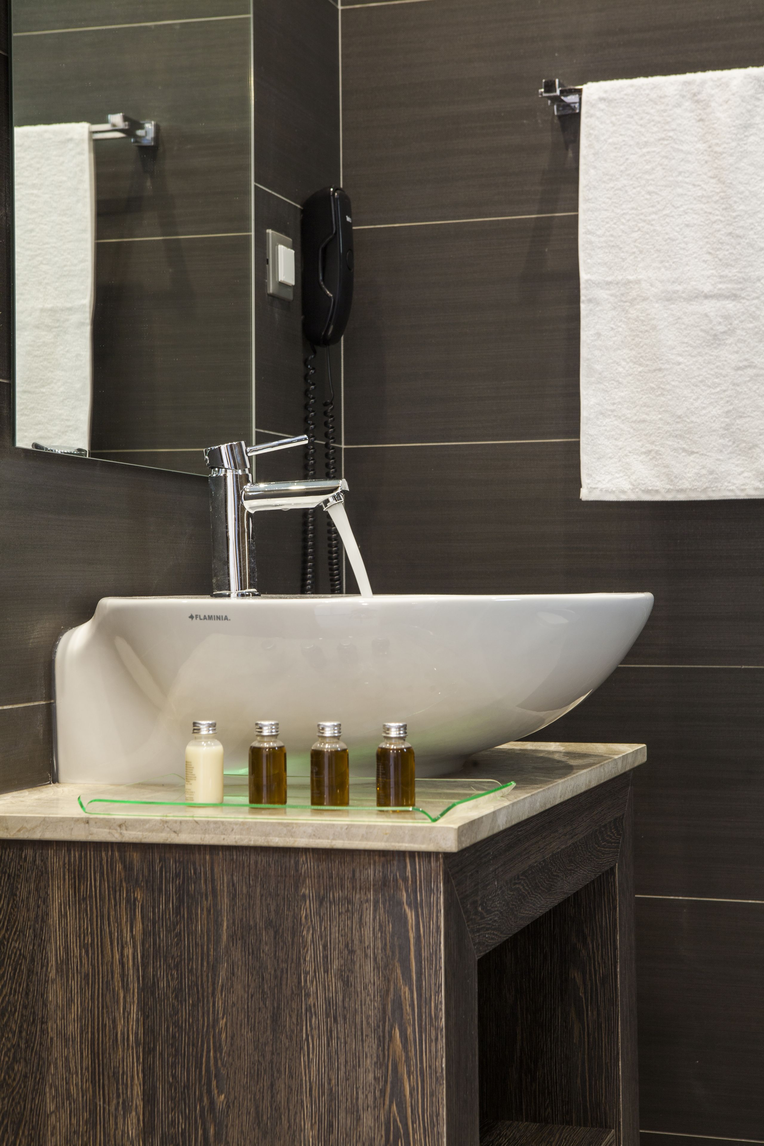 A bathroom with a white sink, a mirror, a telephone, and a towel hanging on the wall.