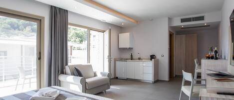 A modern hotel room with a bed, a sofa, a dining table, and a kitchen area.