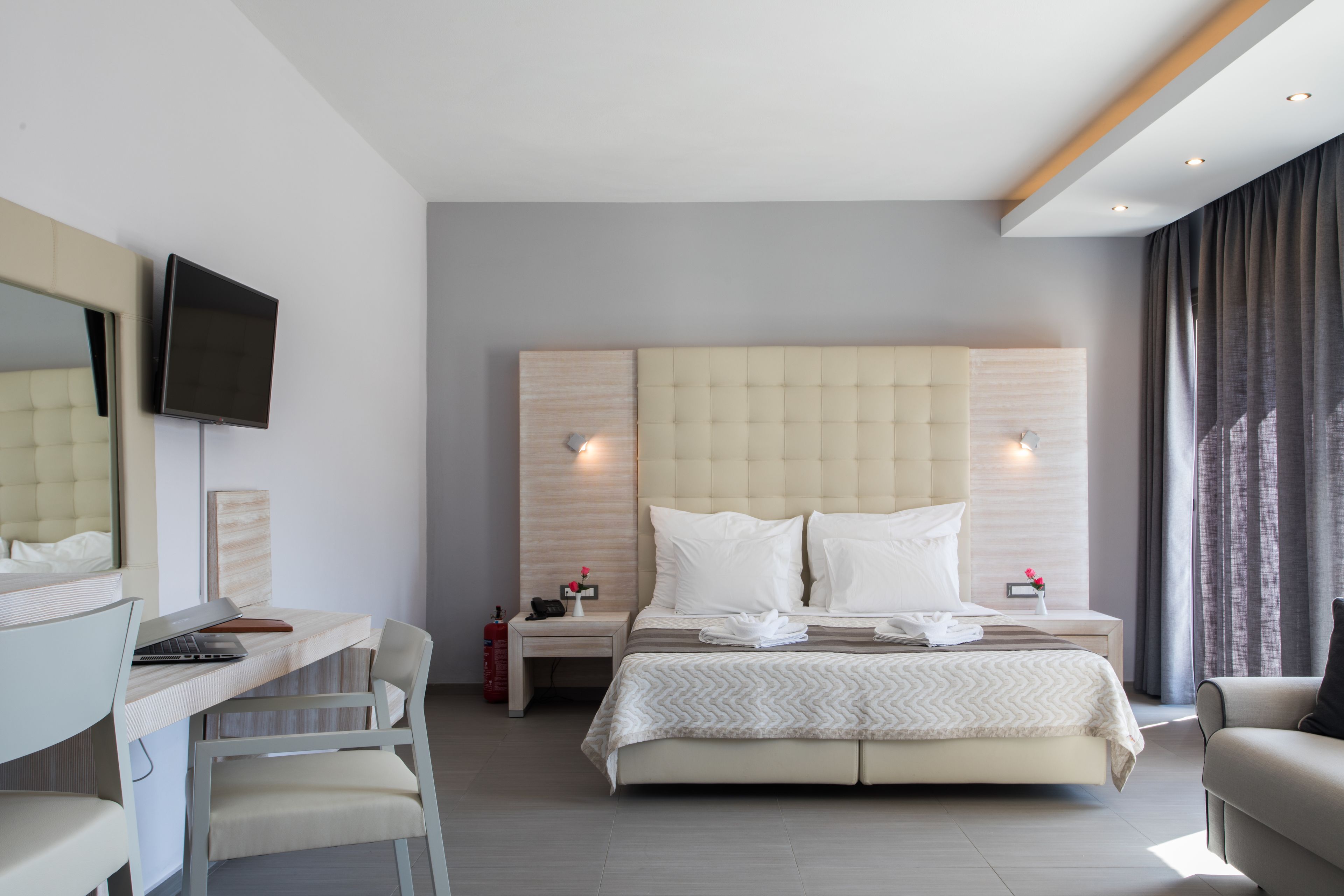 Una habitación de hotel moderna con una cama grande, un escritorio con una computadora portátil, una silla y un televisor montado en la pared.