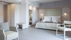 A modern hotel room with a large bed, two white chairs, a small table, and a mirror. - Aqua Oliva Resort (Igoumenitsa)