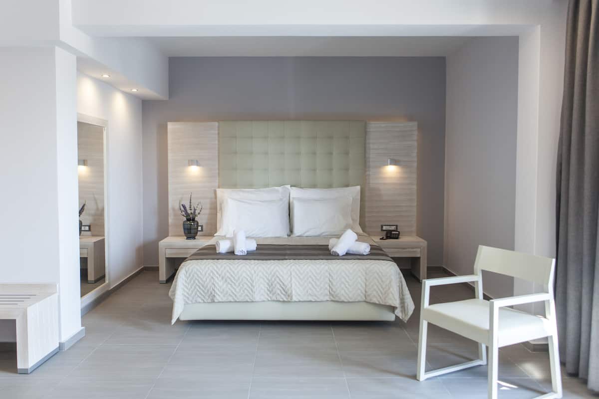 A modern hotel room with a large bed, a bedside table, a chair, and a mirror.