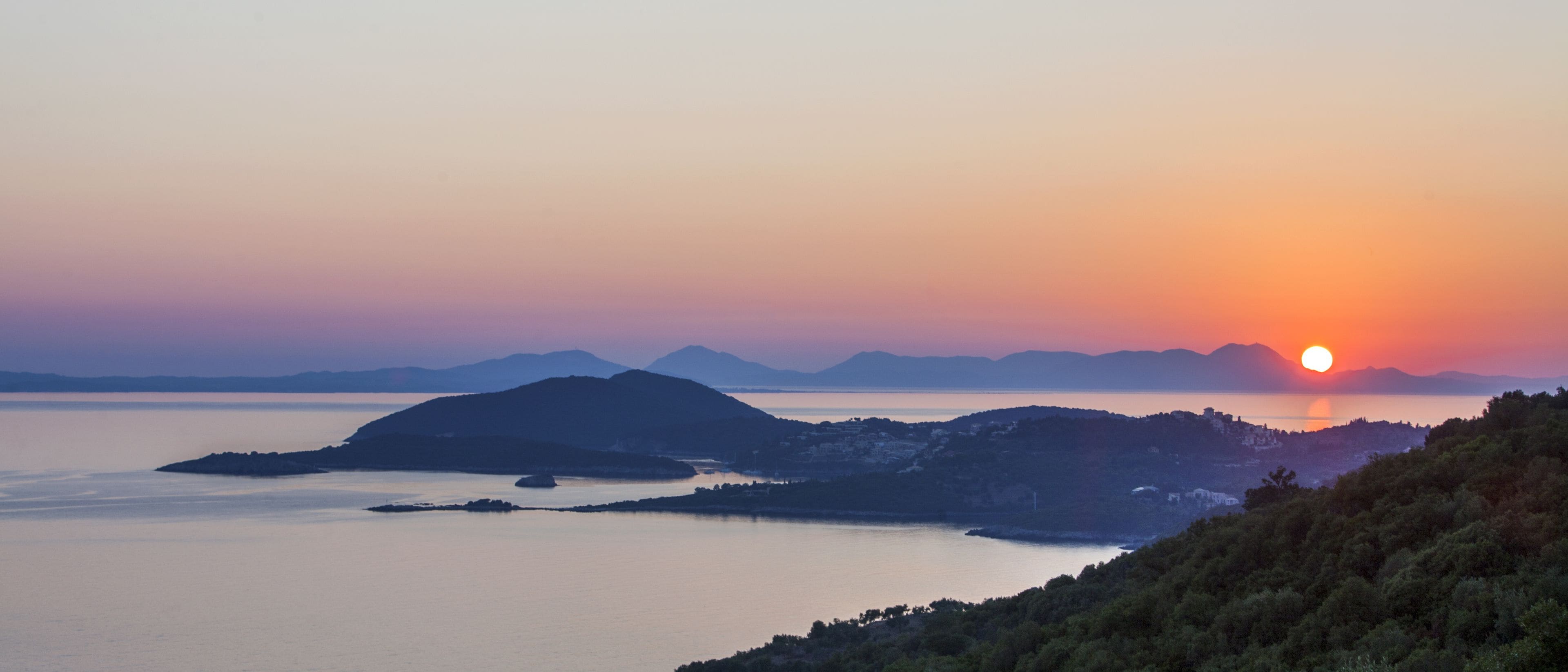 A coastal landscape with a sunset over water and hills.