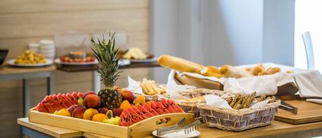 A buffet table with various fruits, bread, and a pineapple.