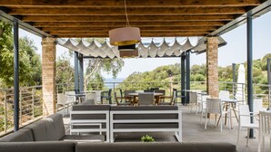 An outdoor patio with a wooden pergola, seating area, and tables. - Aqua Oliva Resort (Igoumenitsa)