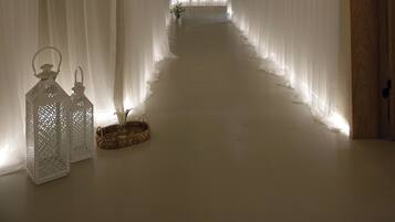 A corridor with sheer white drapes, a wooden door, and two lanterns on the floor.