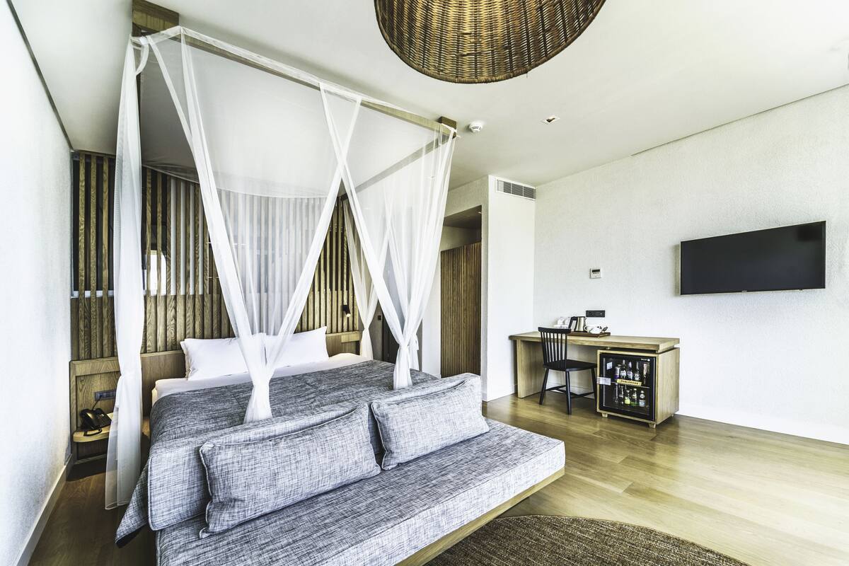 A modern bedroom with a bed, a sofa, a desk, and a television.