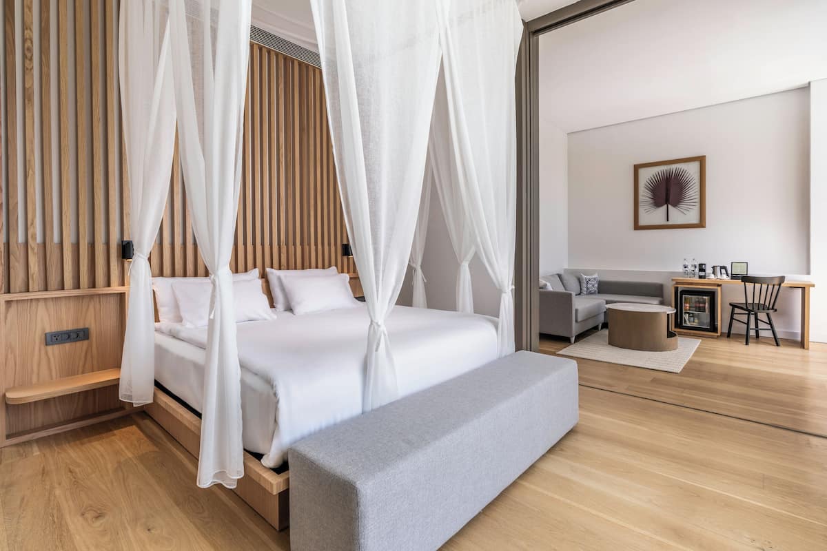 A modern bedroom with a canopy bed, a grey sofa, a small table, and a bench.