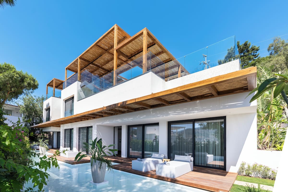 A modern two-story house with a large glass balcony, a swimming pool, and outdoor seating.