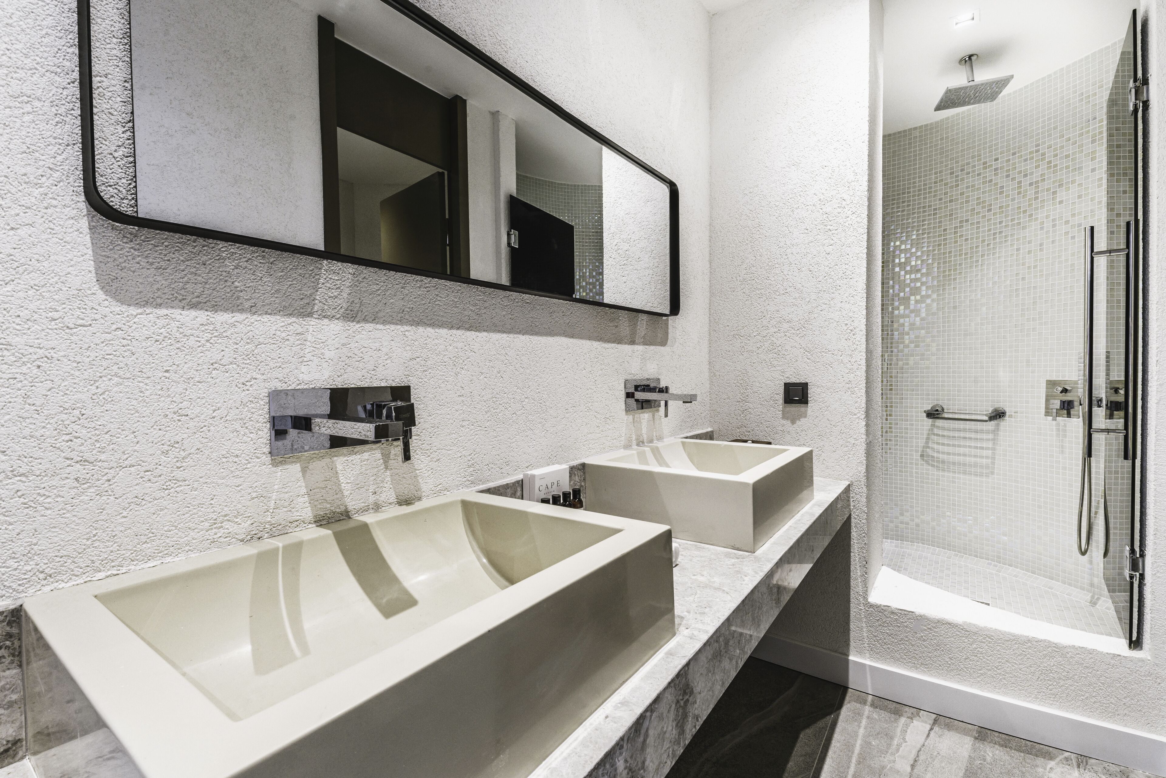 A modern bathroom with two sinks, a large mirror, and a walk-in shower.