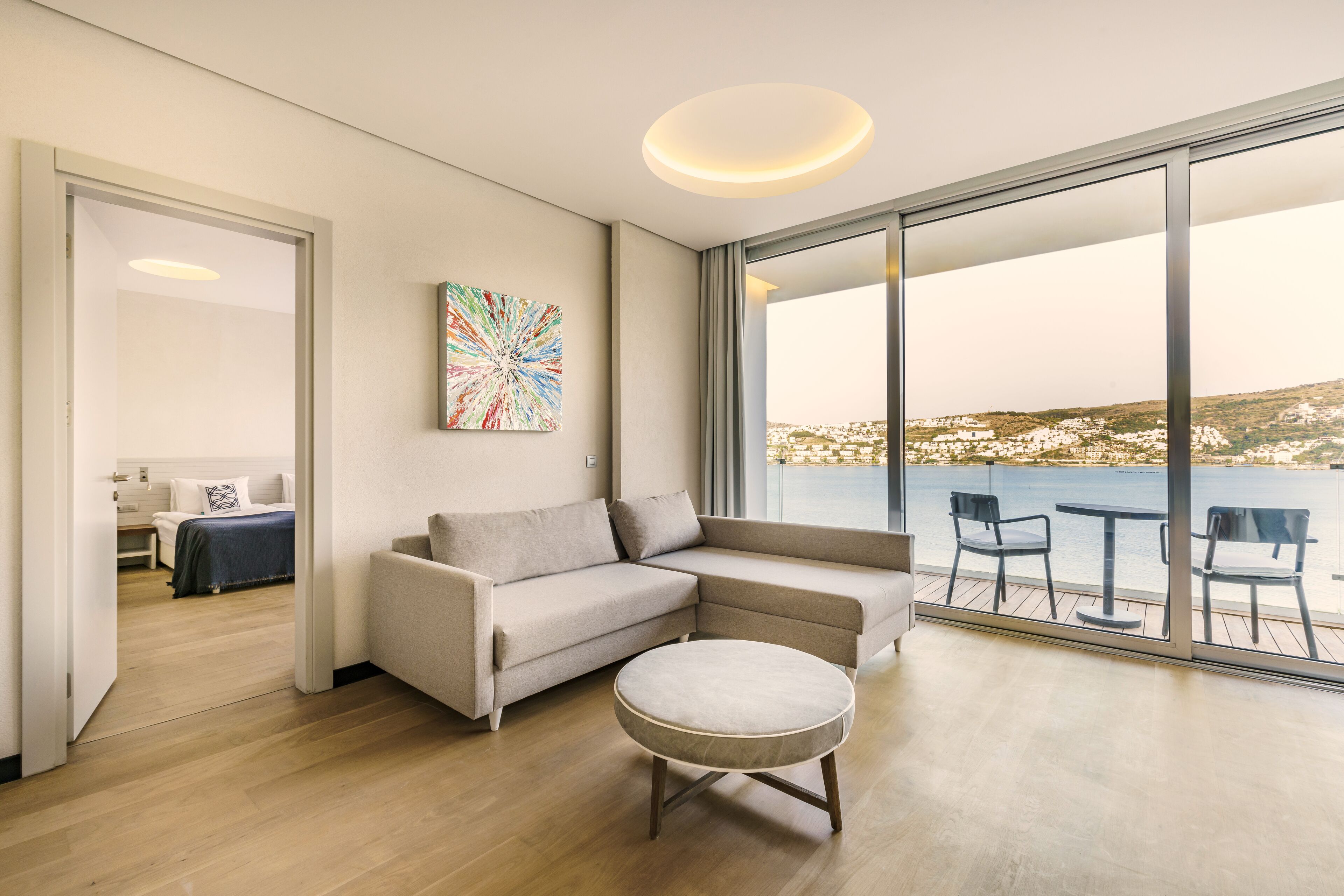 A modern living room with a sofa, ottoman, and a view of the sea.