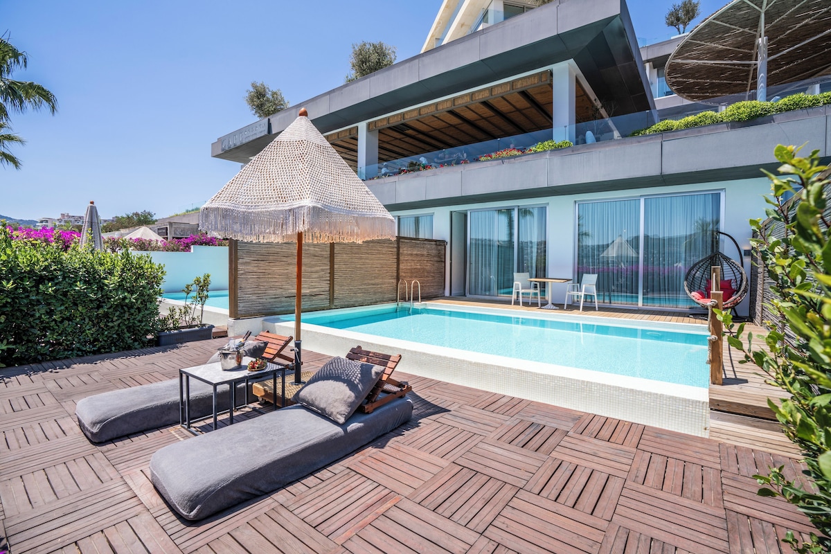 A modern outdoor pool area with lounge chairs, a table, and a decorative umbrella.