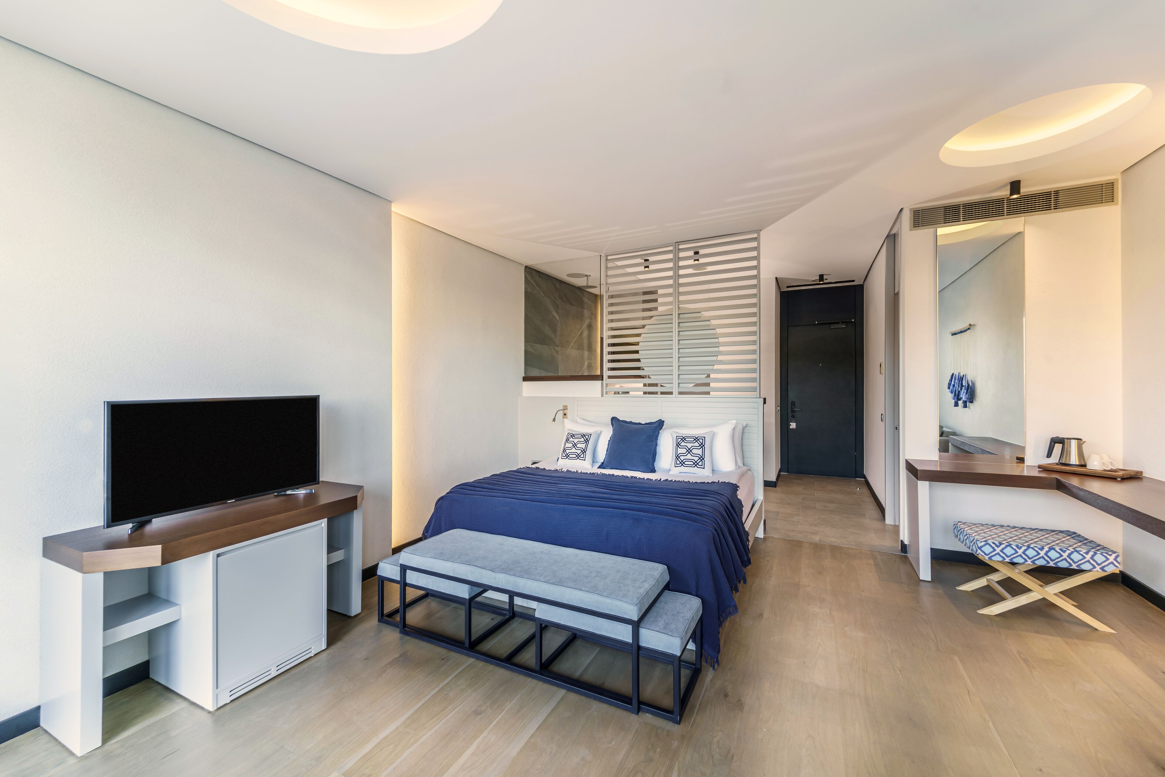 Un dormitorio moderno con cama, televisor, banca y escritorio.