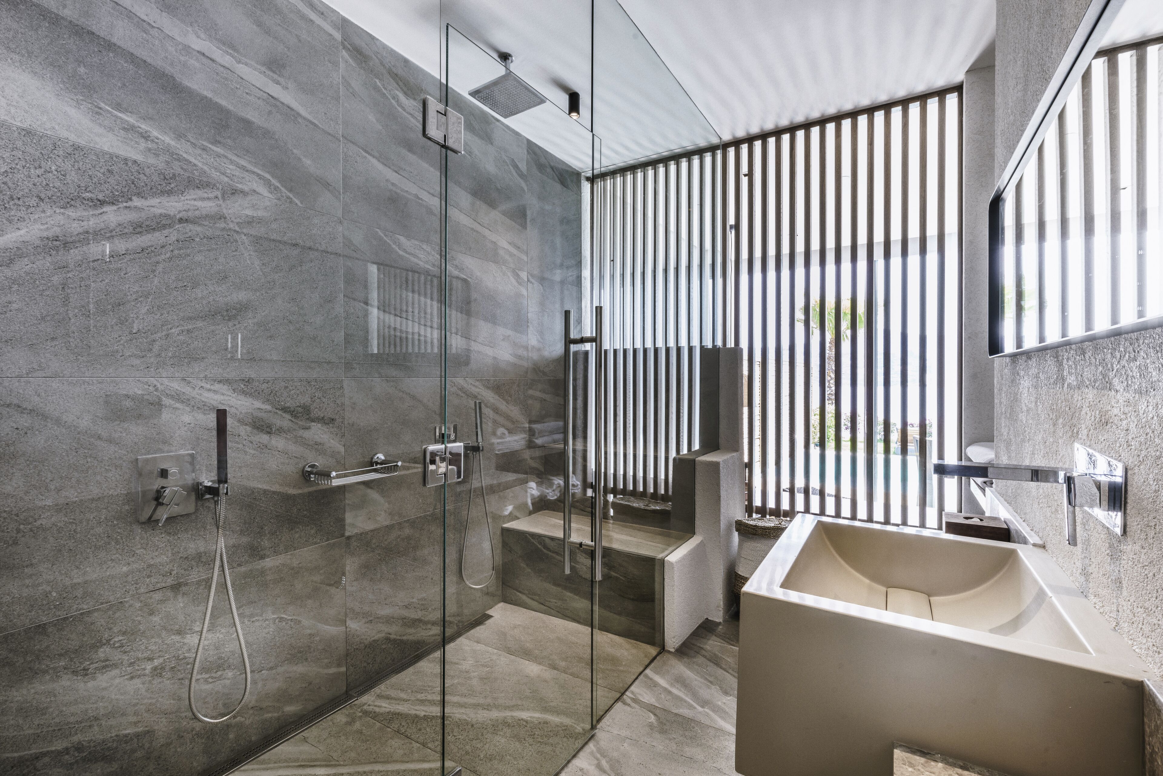 A modern bathroom with a glass-enclosed shower, a large sink, and a view through vertical blinds.