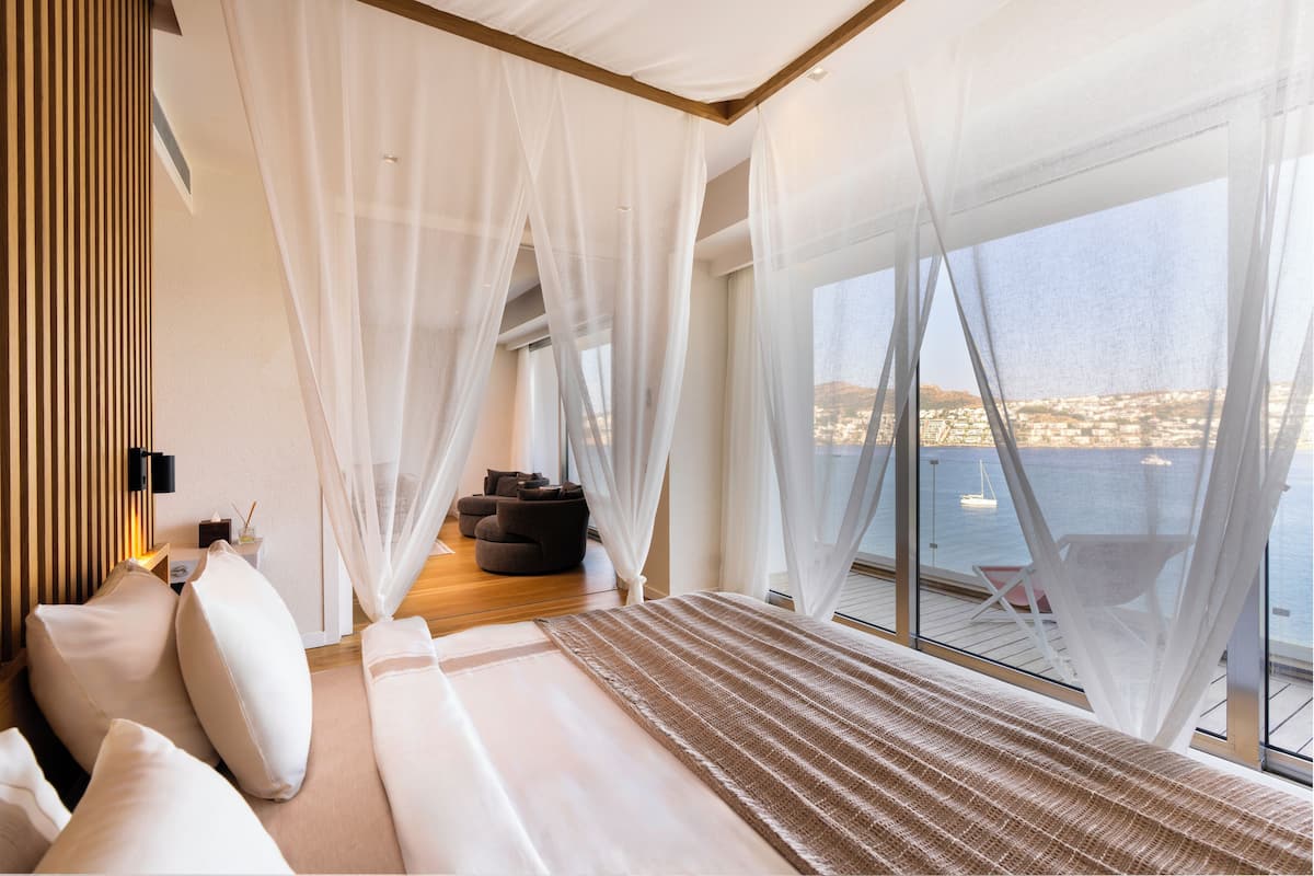 A bedroom with a large bed, a view of the sea, and a balcony with a chair.