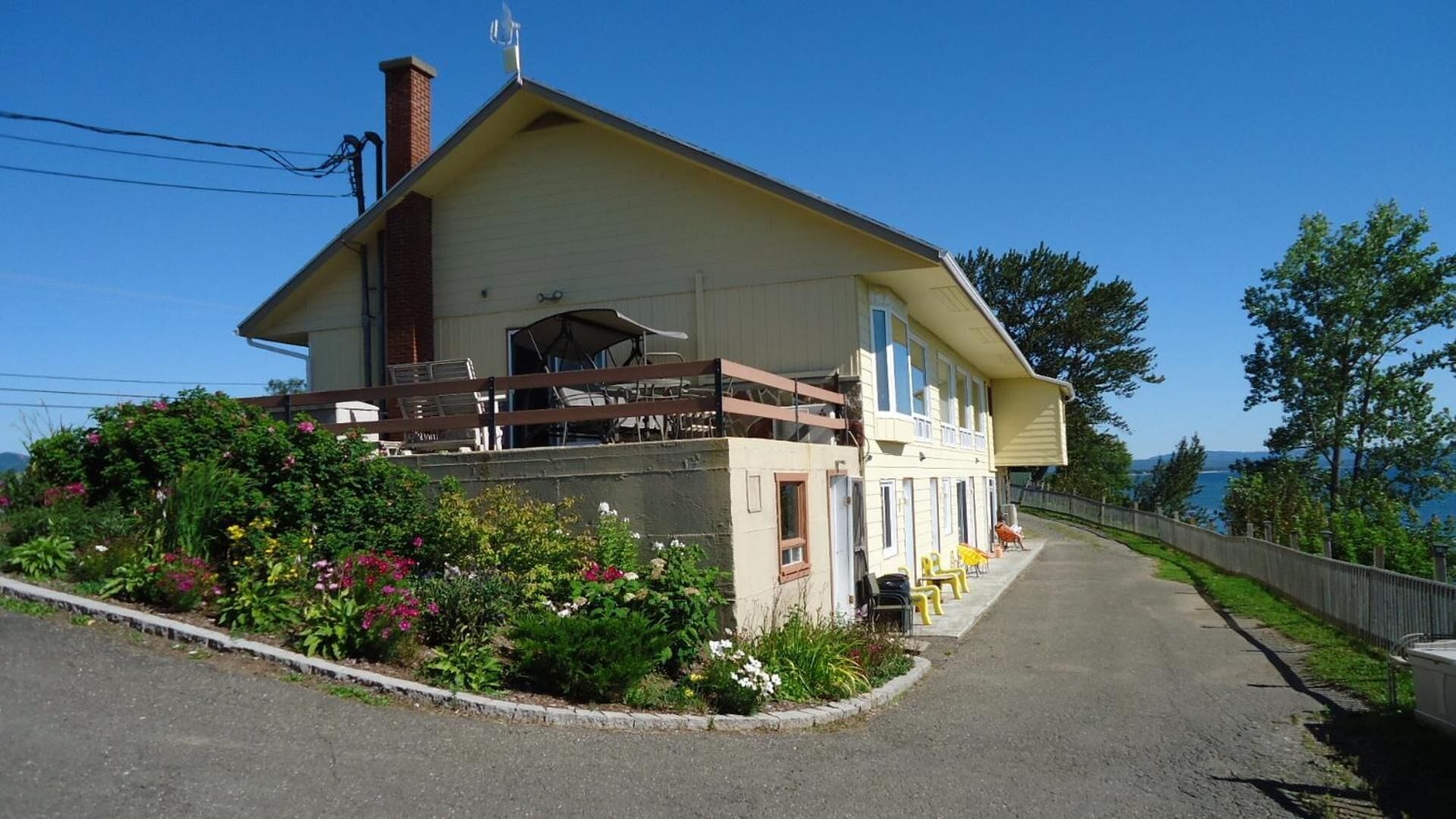 A two-story building with a balcony, surrounded by lush greenery and a clear view of the sky.
