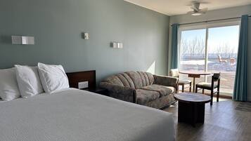 A hotel room with a large bed, a sofa, a small table, and a view of a snowy landscape through the window.