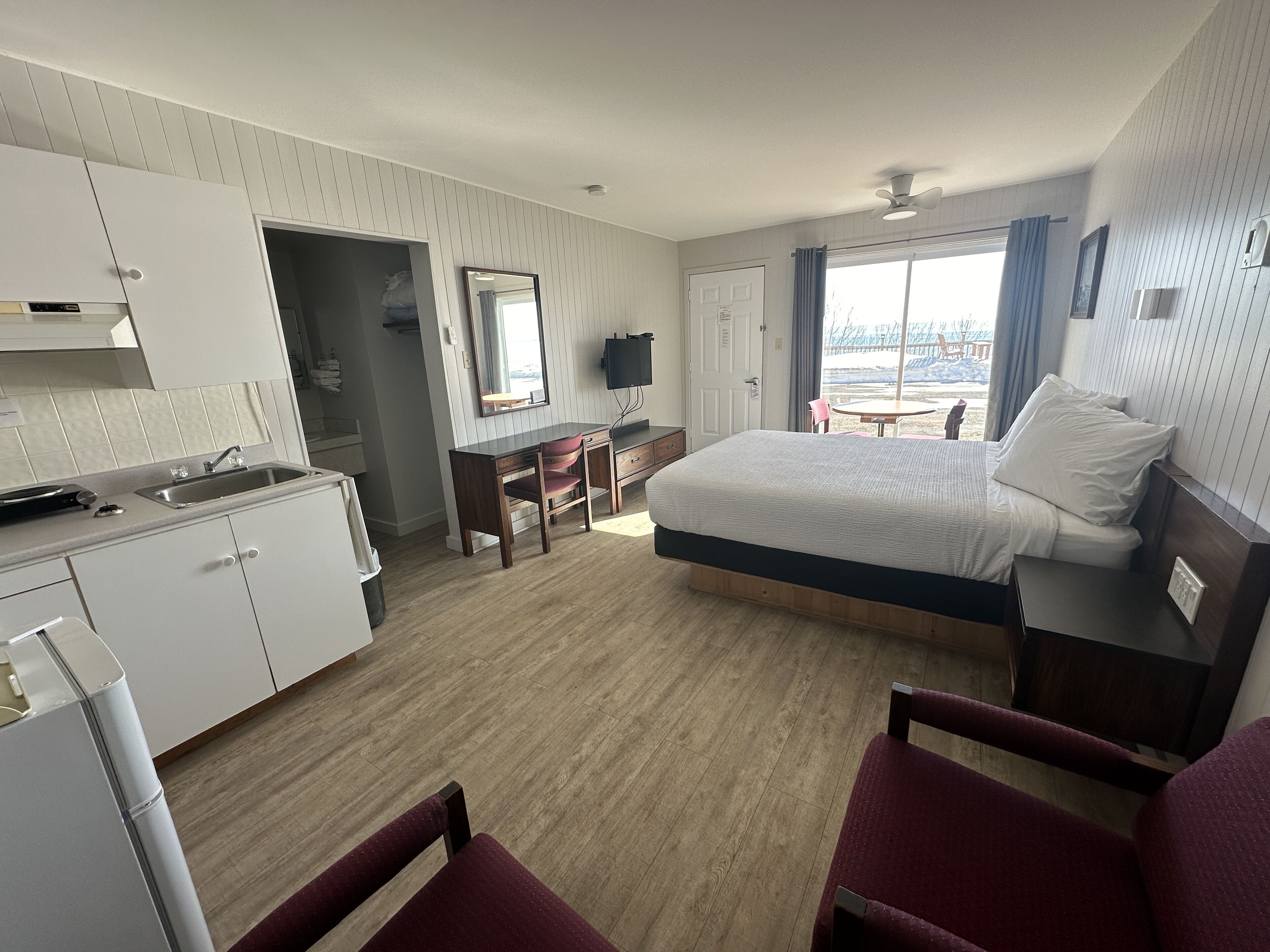 Habitación de hotel con cama, escritorio, silla, mesita, televisor y ventana con cortinas.