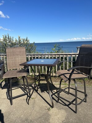 A patio with two wicker chairs and a small table, overlooking a body of water.