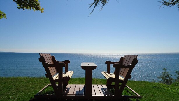 Two wooden Adirondack chairs facing a body of water with a clear sky. - Motel Carleton sur mer (Carleton-sur-Mer)
