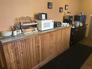 A reception area with a wooden counter, a microwave, a coffee machine, and various food items.