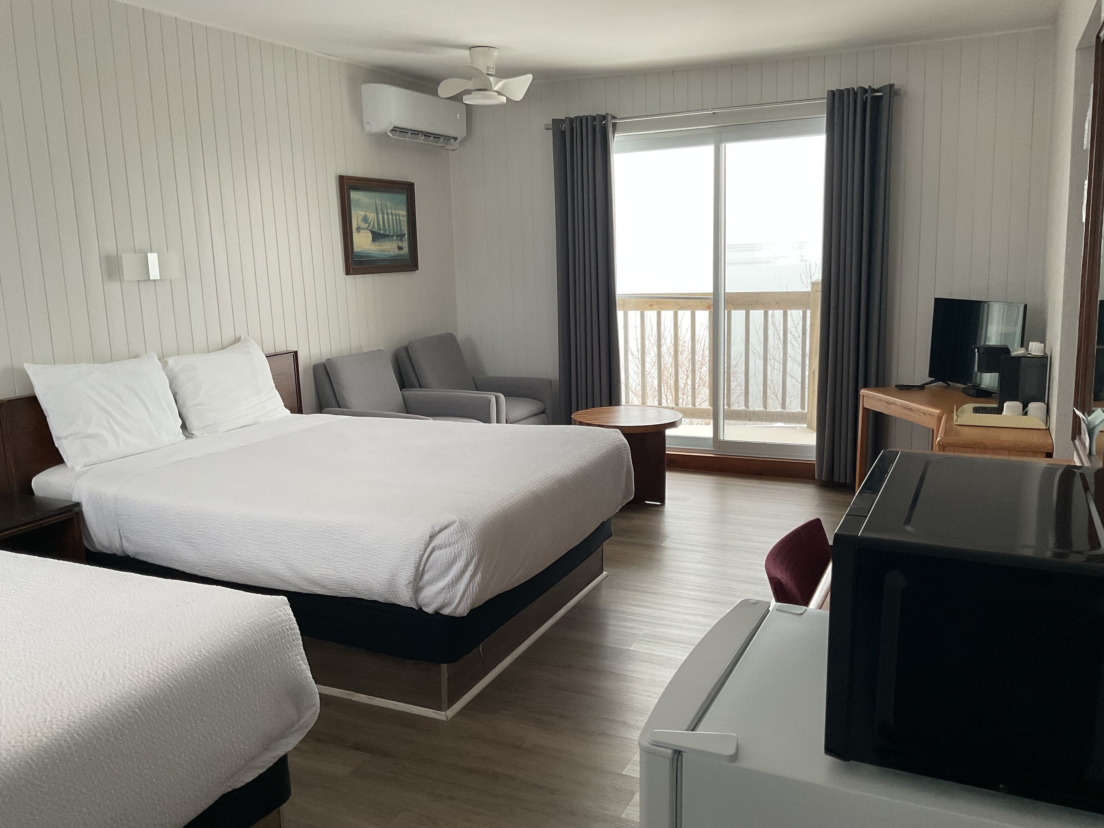 A hotel room with a large bed, a desk with a computer, a TV, and a balcony with a view of the outside.