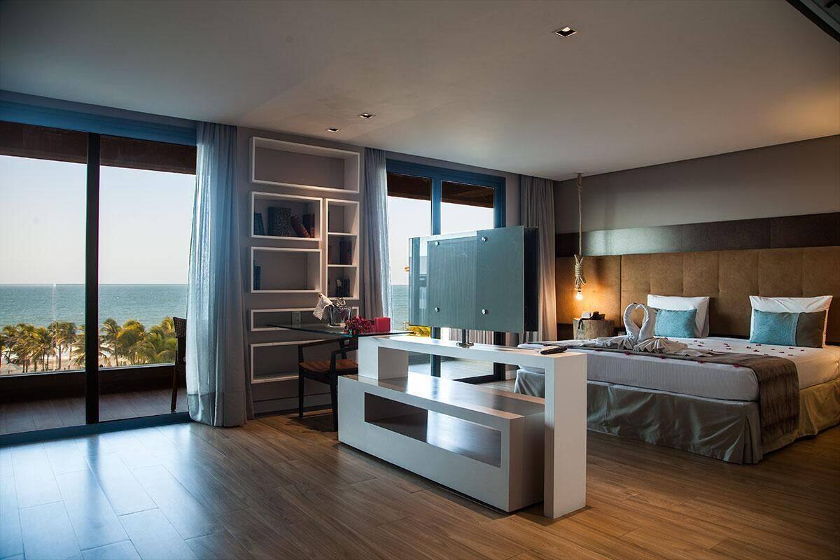 Habitación de hotel moderna con un ventanal grande, una cama, un televisor, un escritorio y vistas al océano.