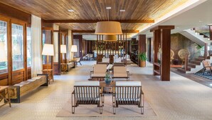 Un hall espacioso con una zona de estar central, techo de madera y grandes ventanales.