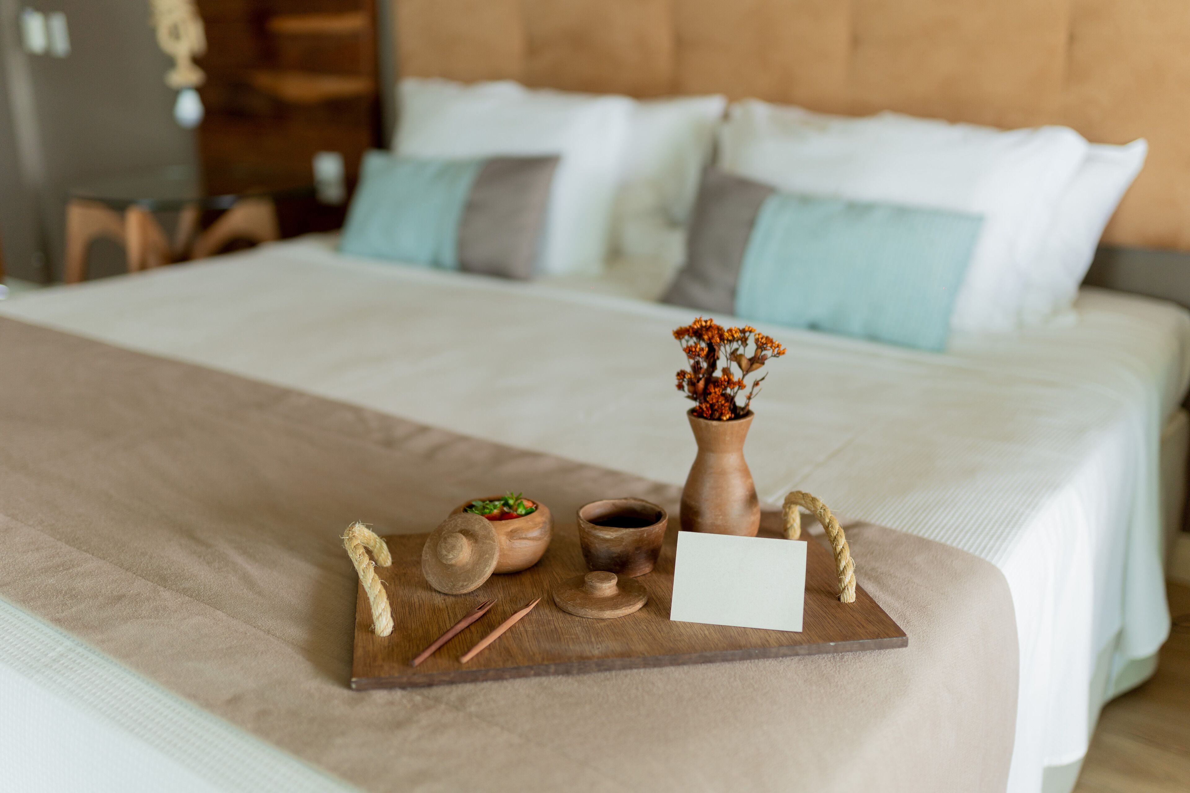 A neatly made bed with a wooden tray holding a vase, a bowl, and chopsticks.
