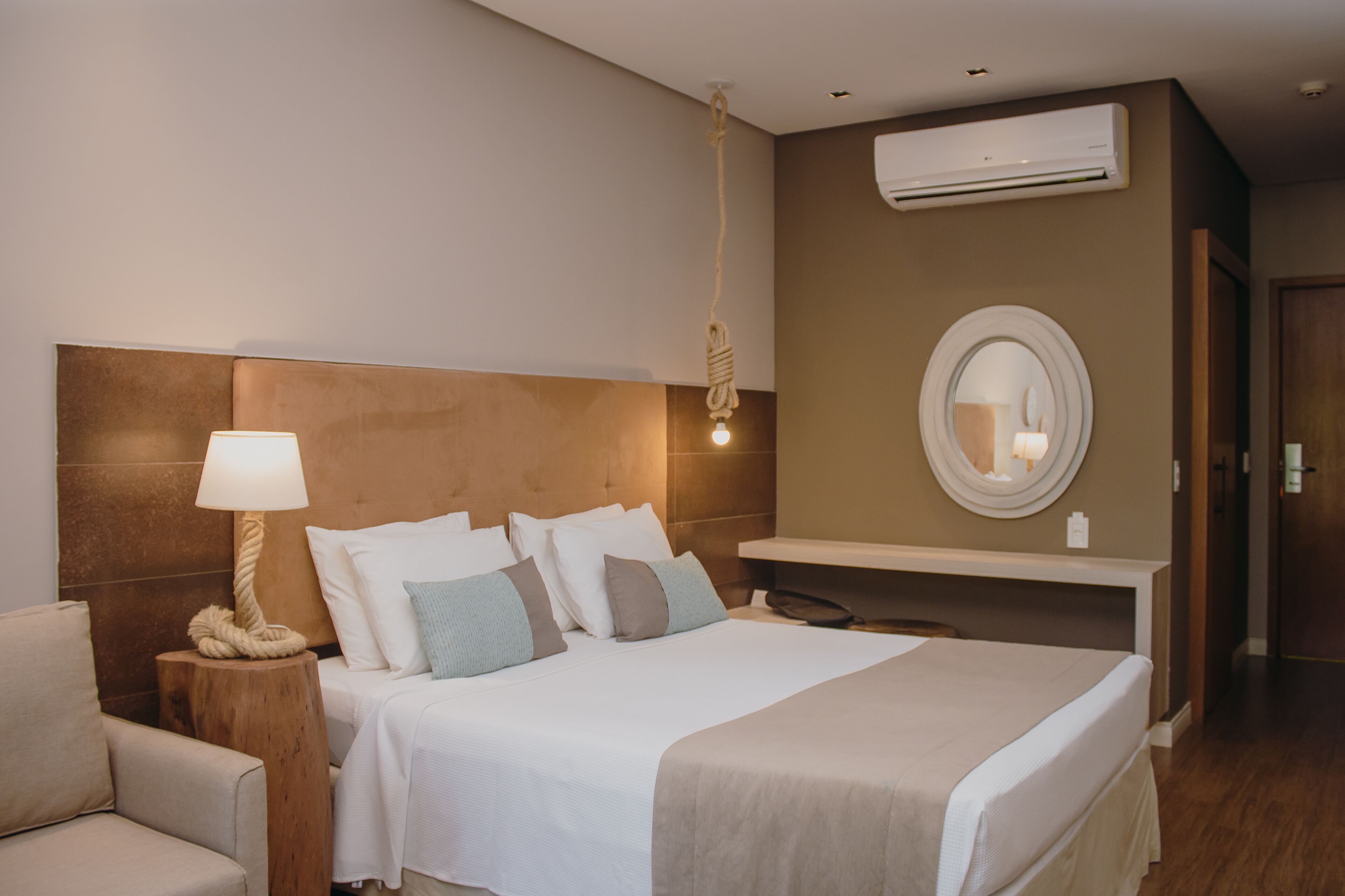 Habitación de hotel con cama, lámpara de noche y un espejo redondo en la pared.