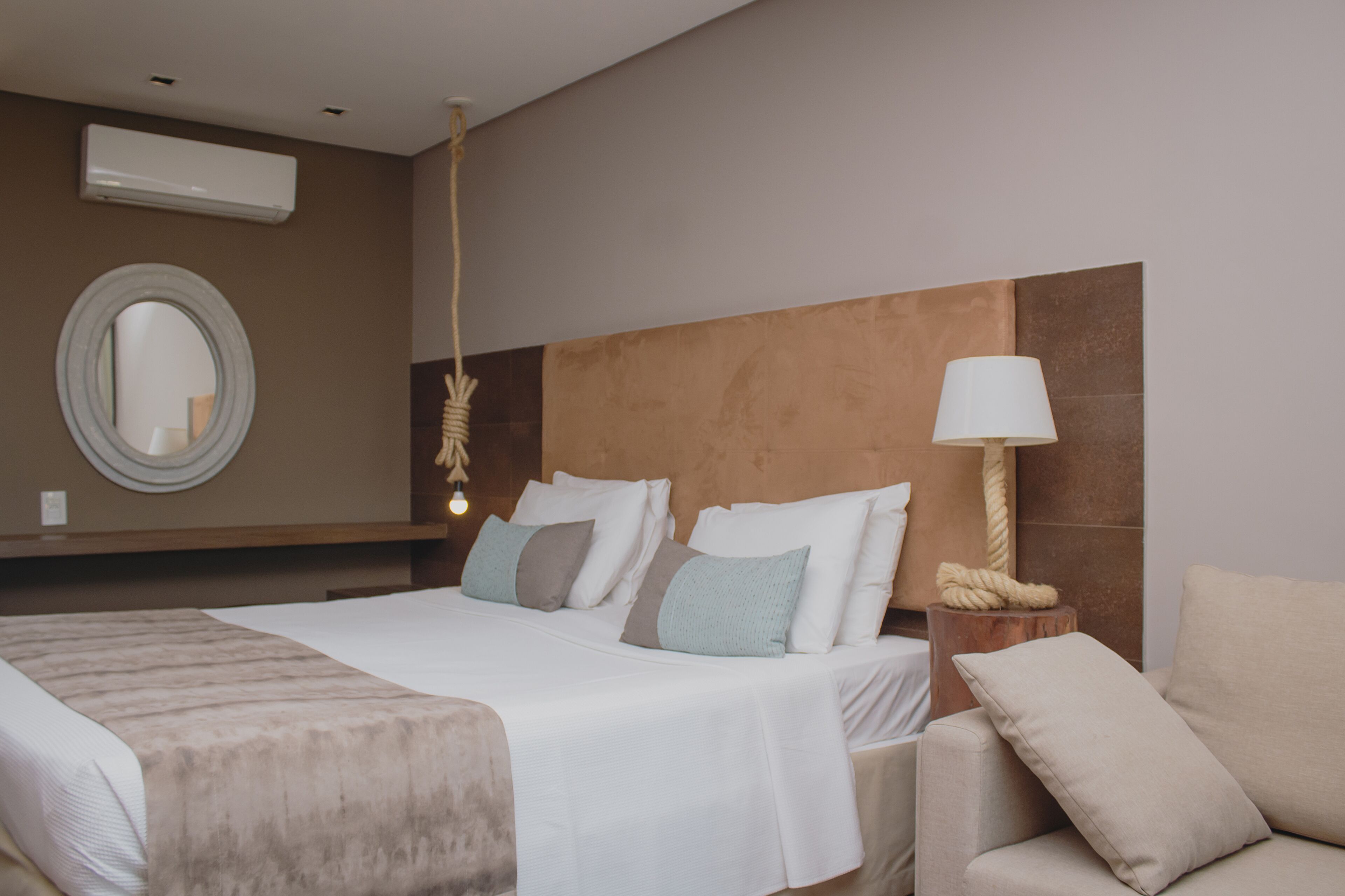 A hotel room with a large bed, a round mirror, a bedside lamp, and a wooden headboard.