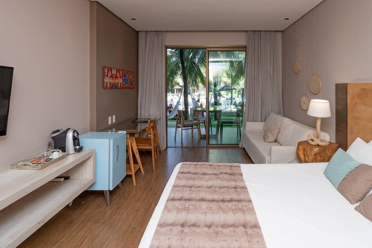 Habitación de hotel con cama, televisor, escritorio con silla, sofá y vistas al exterior.