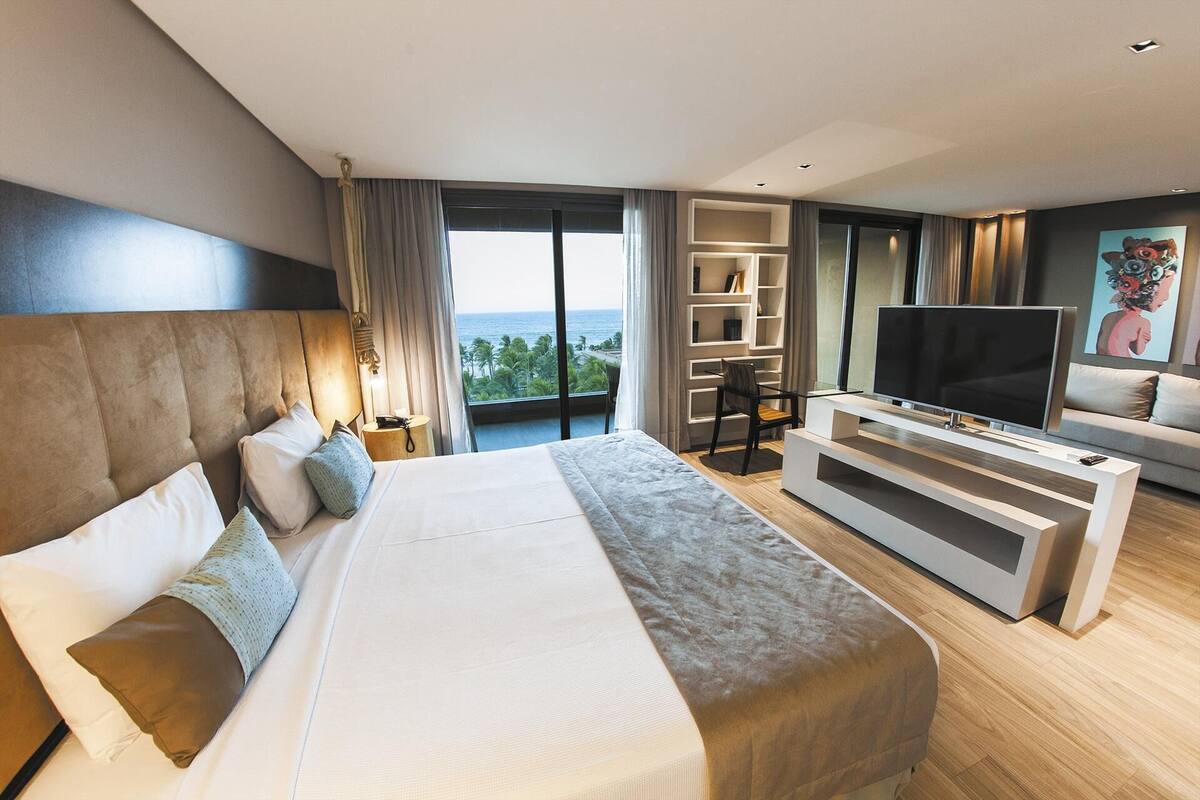 Una habitación de hotel moderna con una cama grande, televisión, zona de estar y vista al océano.