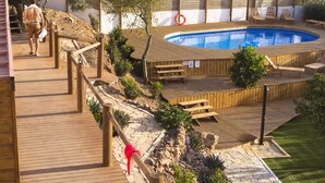 Eine Holzterrasse führt zu einem Schwimmbecken mit einem Rettungsring, umgeben von Grünpflanzen und einer Steinmauer.