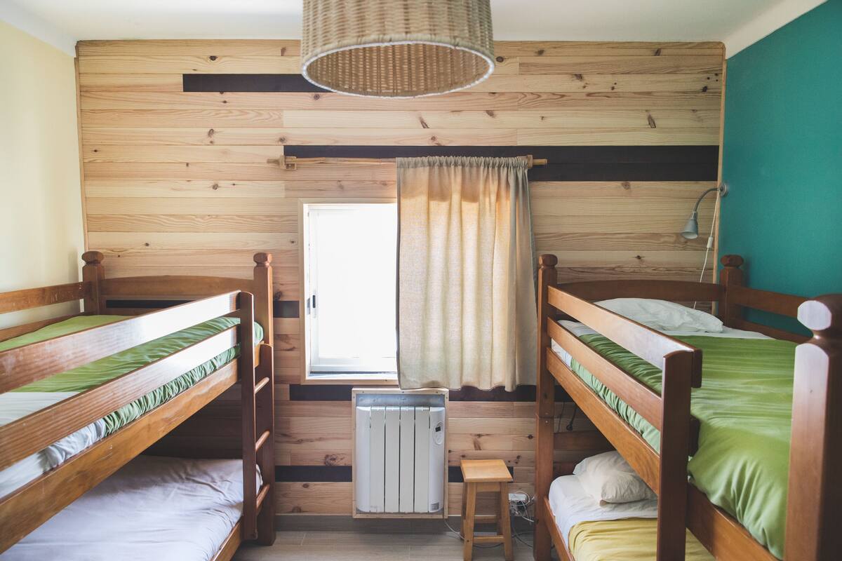 Une pièce avec trois lits superposés, une fenêtre avec des rideaux, un radiateur et un luminaire suspendu.