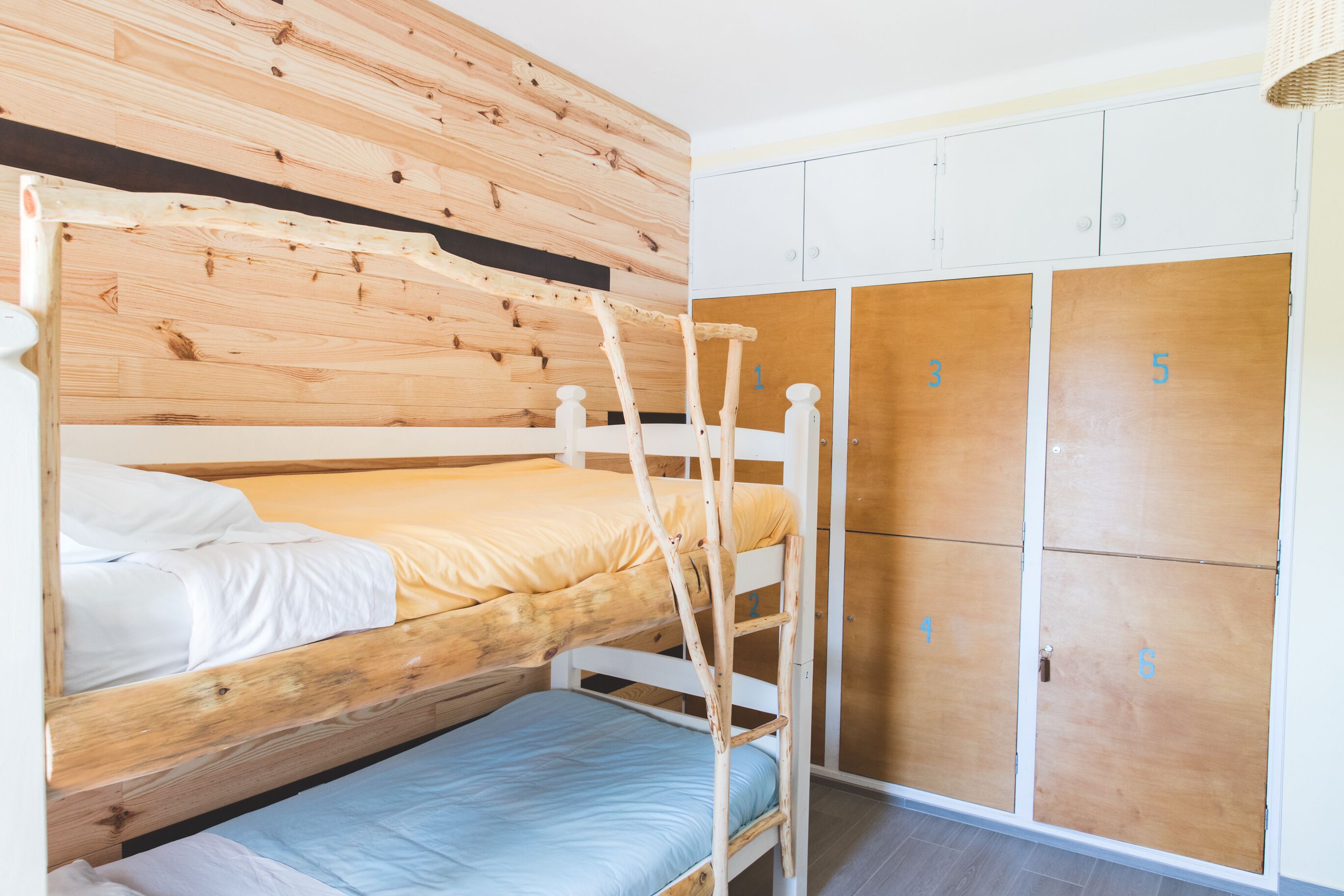 Une chambre avec un lit superposé doté d’une tête de lit en bois, d’une échelle et d’une armoire dont les portes sont numérotées.