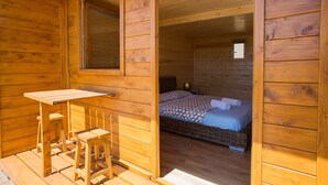 Eine Holzhütte mit einem Einzelbett, einem kleinen Tisch und einer Bank.