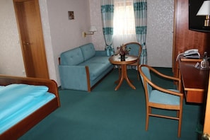 A hotel room with a bed, a sofa, a round table with a lamp, a chair, and a TV. - Gästehaus Wild (Oberasbach)